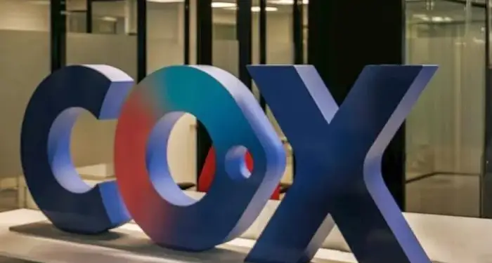 Letras volumétricas tridimensionales con el nombre Cox en una mesa dentro de una oficina corporativa.