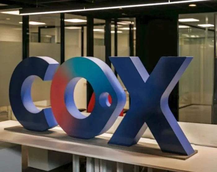 Letras volumétricas tridimensionales con el nombre Cox en una mesa dentro de una oficina corporativa.