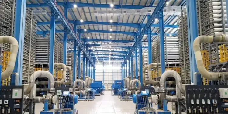 Vista interior de una gran planta industrial con estructuras metálicas azules y complejos sistemas de tuberías y maquinaria.