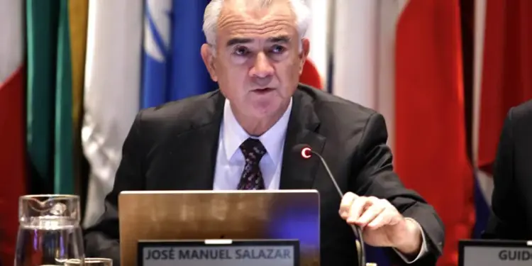 Hombre de cabello gris en traje y corbata, hablando en una conferencia. Se ve un micrófono, un portátil y una placa con 'JOSÉ MANUEL SALAZAR, SECRETARIO EJECUTIVO, CEPAL'. Banderas al fondo.