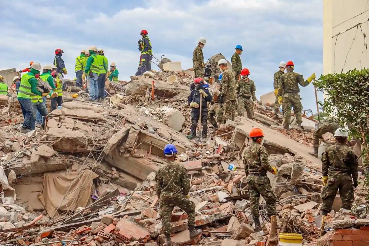 Personal de rescate y voluntarios con cascos trabajando entre los escombros de un edificio derrumbado.