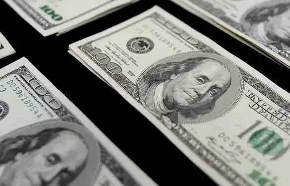 Varios fajos de billetes de cien dólares estadounidenses distribuidos sobre una superficie oscura.