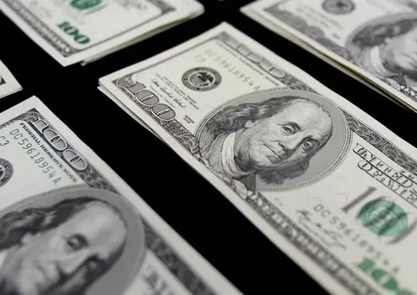 Varios fajos de billetes de cien dólares estadounidenses distribuidos sobre una superficie oscura.