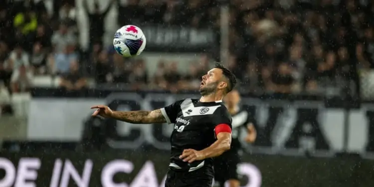 Jugador de fútbol con uniforme negro y blanco controlando el balón con el pecho durante un partido bajo la lluvia.