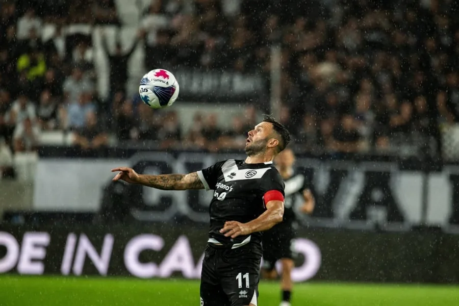Jugador de fútbol con uniforme negro y blanco controlando el balón con el pecho durante un partido bajo la lluvia.