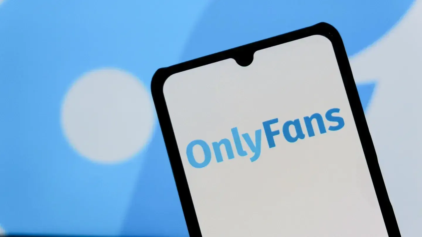 Logotipo azul de OnlyFans visible en la pantalla blanca de un smartphone con fondo azul difuminado.