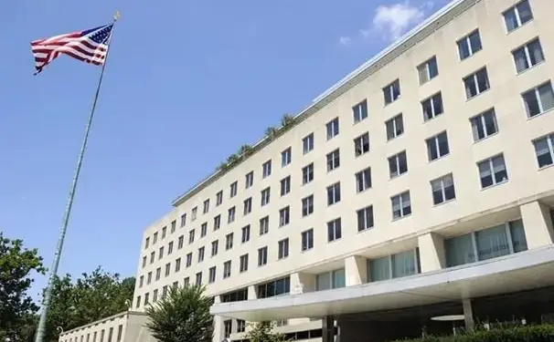 Vista exterior del Edificio Harry S Truman con la bandera de Estados Unidos ondeando. Un edificio oficial de múltiples pisos con ventanas.
