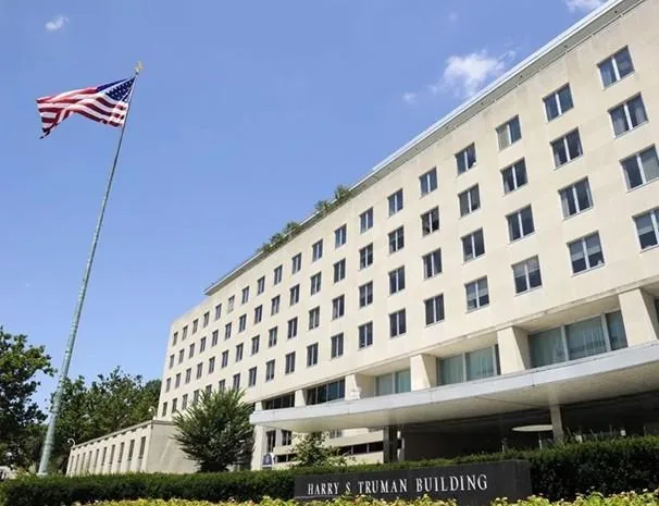 Vista exterior del Edificio Harry S Truman con la bandera de Estados Unidos ondeando. Un edificio oficial de múltiples pisos con ventanas.