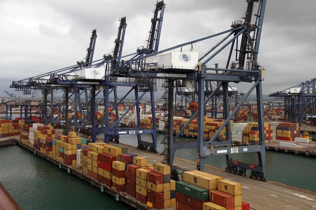 Grúas de pórtico industriales operando en un puerto marítimo con contenedores apilados en el muelle.