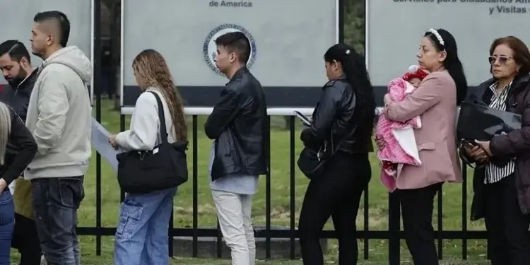 Grupo de personas esperando en una fila frente a los carteles de la Embajada de los Estados Unidos de América.