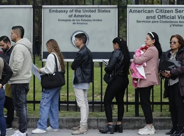 Grupo de personas esperando en una fila frente a los carteles de la Embajada de los Estados Unidos de América.