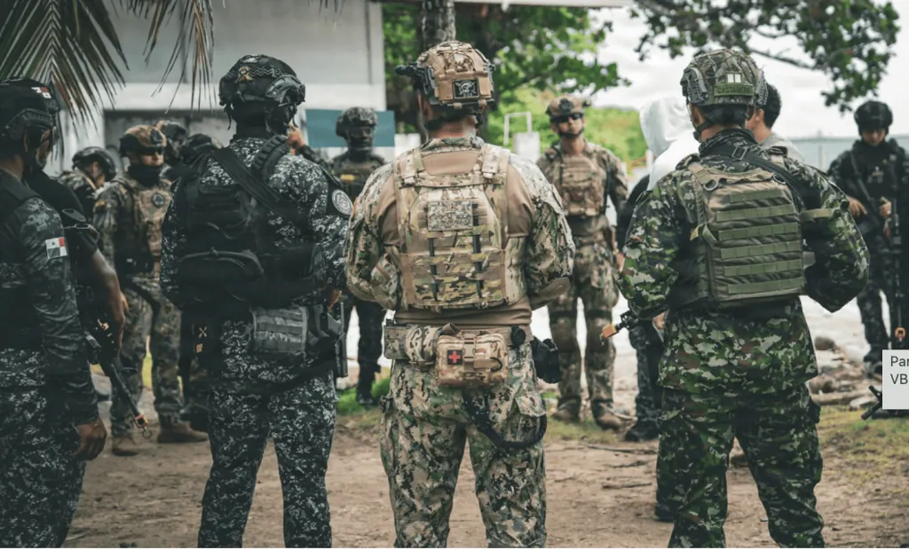 Grupo de fuerzas especiales uniformados con equipo táctico y cascos en un área exterior al aire libre.