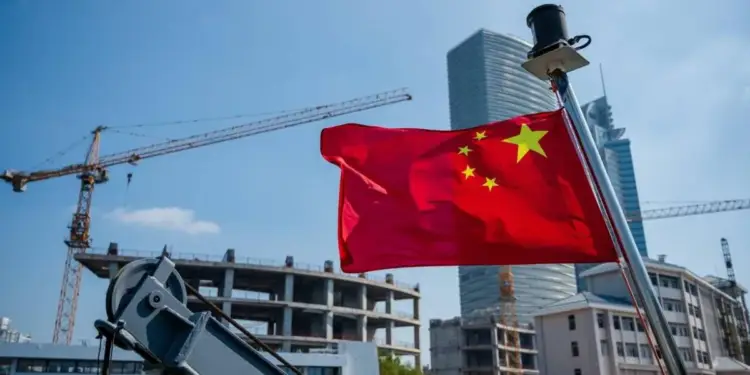 Bandera de China ondeando frente a edificios en construcción y grúas en un entorno urbano.