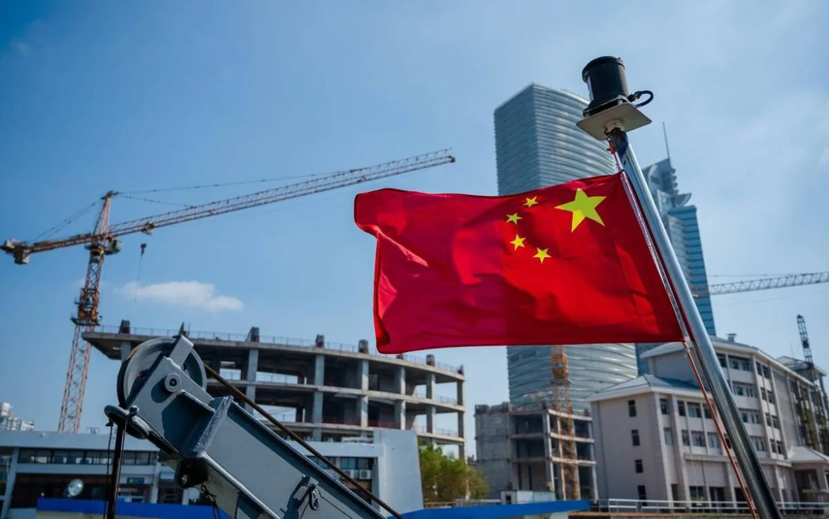 Bandera de China ondeando frente a edificios en construcción y grúas en un entorno urbano.