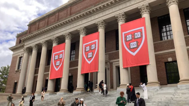 Fachada de la Biblioteca Widener de Harvard con banderas rojas del escudo universitario. Estudiantes en las escaleras.