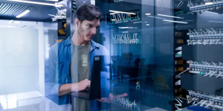 Técnico informático usando una laptop frente a servidores en un centro de datos