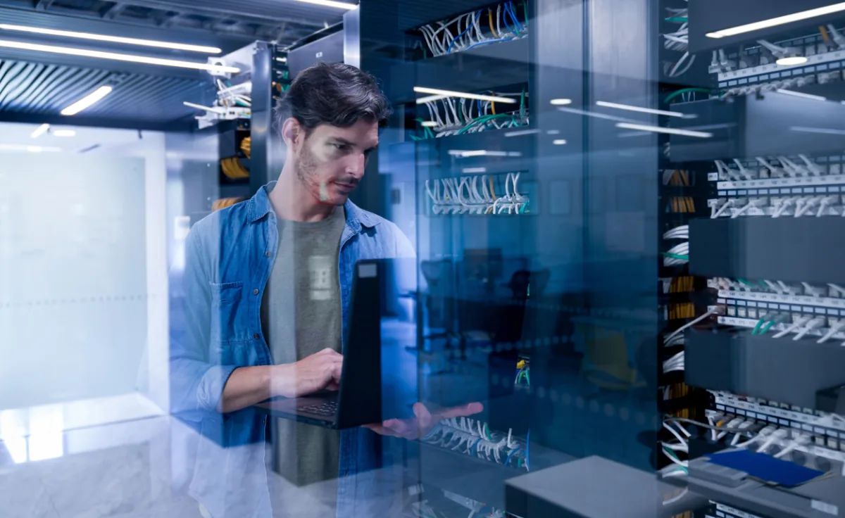 Técnico informático usando una laptop frente a servidores en un centro de datos