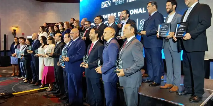 Grupo de profesionales en un evento de negocios recibiendo reconocimientos y premios en el escenario.