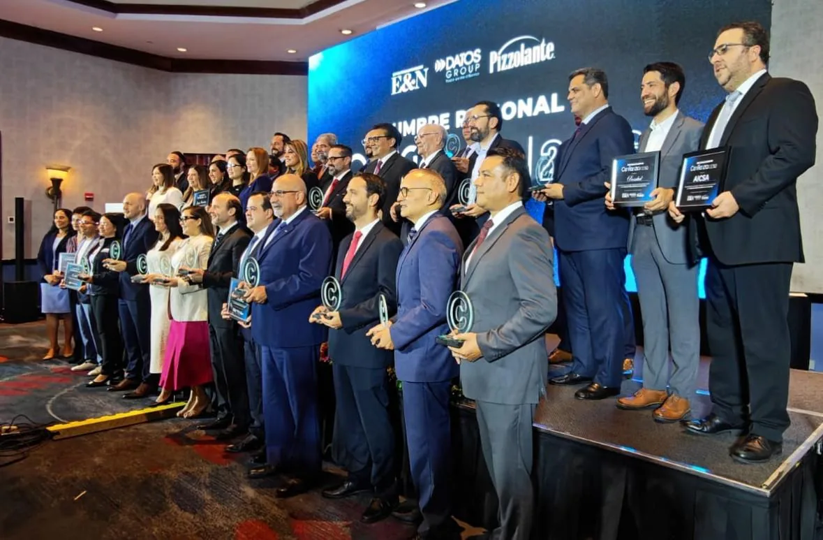 Grupo de profesionales en un evento de negocios recibiendo reconocimientos y premios en el escenario.