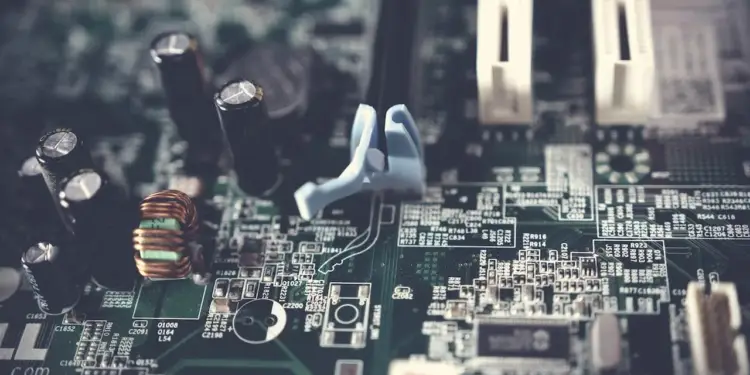 Primer plano de una placa de circuito verde con múltiples componentes electrónicos como condensadores negros, una bobina de cobre y conectores blancos y azules. Representa la tecnología digital.