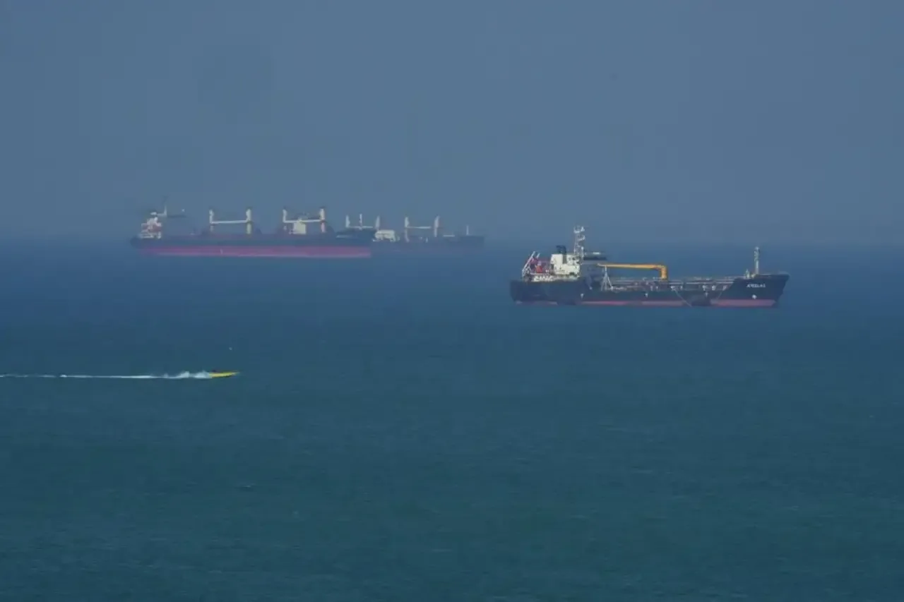 Vista aérea de buques de carga y un tanquero en el mar, con una pequeña embarcación amarilla en primer plano. Representa el comercio marítimo global.