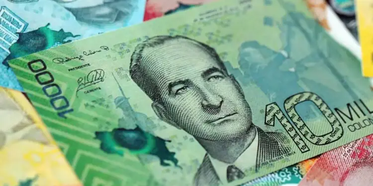 Primer plano de un billete verde de 10000 pesos colombianos con un retrato masculino, firmas y la palabra 'COLOMBIA', sobre otros billetes.