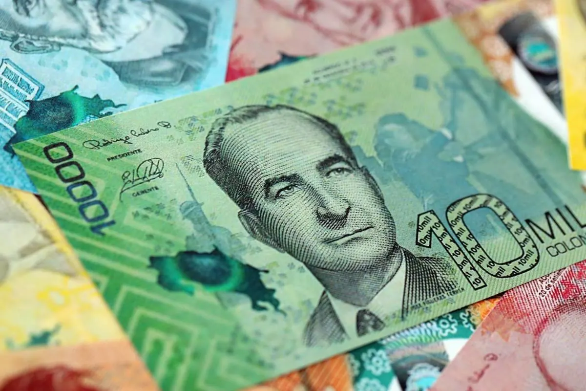 Primer plano de un billete verde de 10000 pesos colombianos con un retrato masculino, firmas y la palabra 'COLOMBIA', sobre otros billetes.