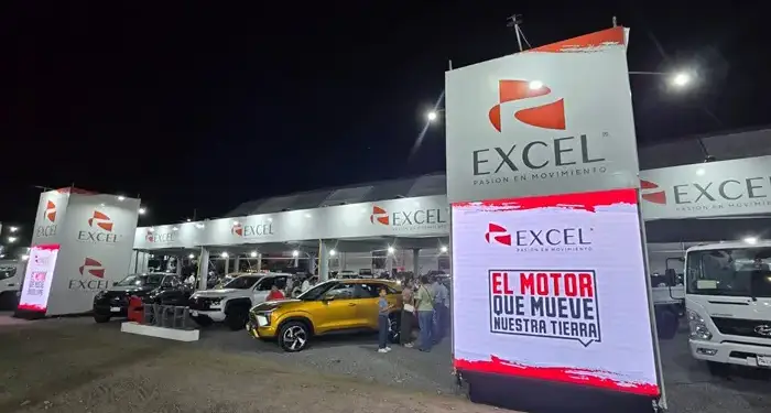 Exhibición nocturna de vehículos nuevos y camiones bajo carpas con logotipos 'Excel'. Varias personas observan los modelos.