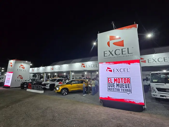 Exhibición nocturna de vehículos nuevos y camiones bajo carpas con logotipos 'Excel'. Varias personas observan los modelos.