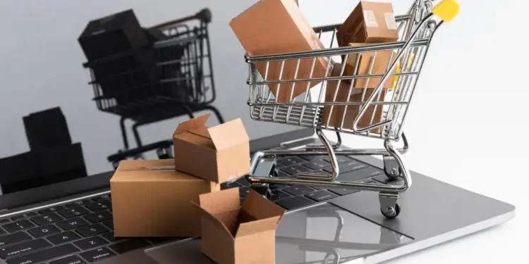 Carritos de compras metálicos pequeños con cajas de cartón sobre el teclado de una computadora portátil.