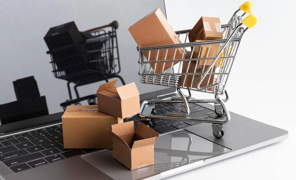 Carritos de compras metálicos pequeños con cajas de cartón sobre el teclado de una computadora portátil.