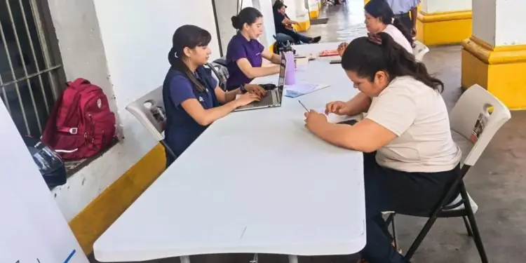 Mujeres registrándose en mesas blancas con laptops y documentos en un evento profesional al aire libre, con un pasillo de fondo.