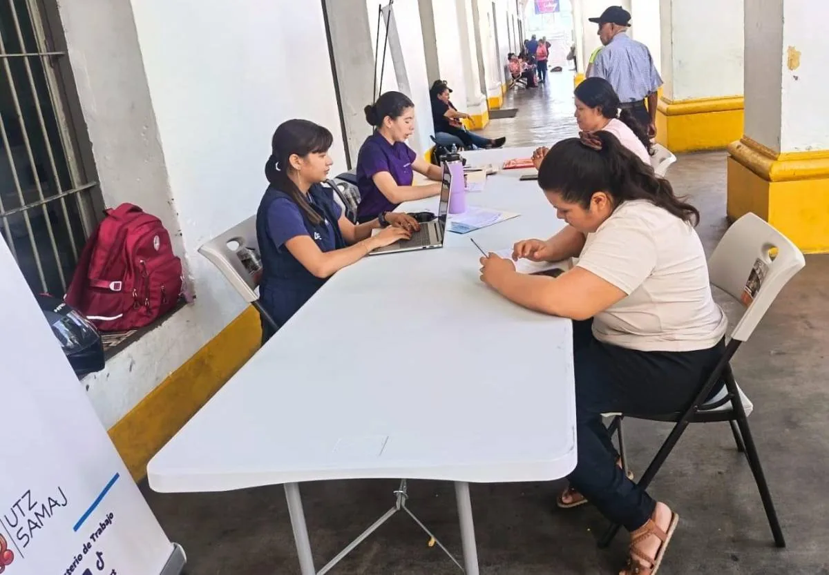 Mujeres registrándose en mesas blancas con laptops y documentos en un evento profesional al aire libre, con un pasillo de fondo.