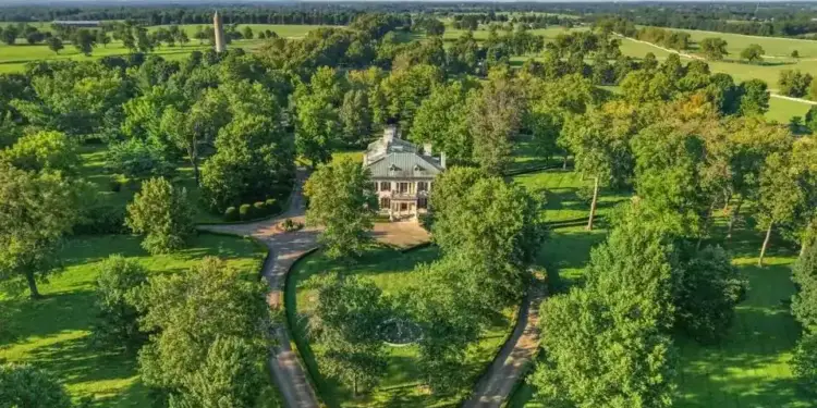 Vista aérea de una gran mansión rodeada de amplios jardines y árboles verdes en una zona rural.