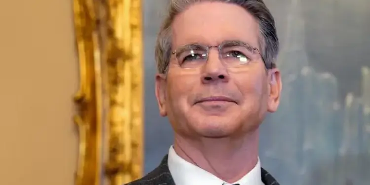 Retrato de un hombre de negocios con anteojos, traje oscuro de rayas diplomáticas y corbata azul en una oficina.