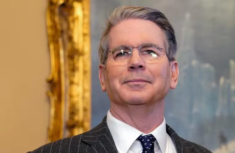 Retrato de un hombre de negocios con anteojos, traje oscuro de rayas diplomáticas y corbata azul en una oficina.