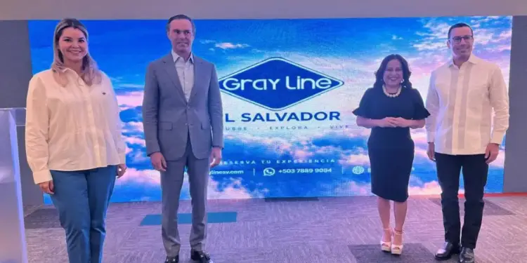 Cuatro personas de pie frente a una gran pantalla azul con el logotipo de Gray Line El Salvador en un evento empresarial.