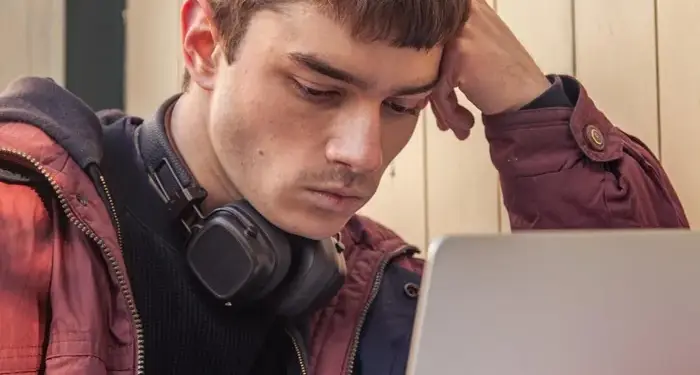 Joven con auriculares al cuello pensativo frente a una laptop en entorno laboral