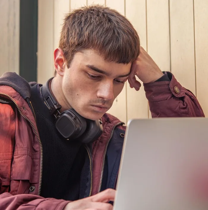 Joven con auriculares al cuello pensativo frente a una laptop en entorno laboral