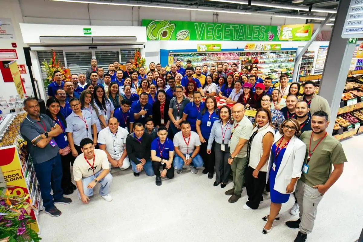 Fotografía grupal de un numeroso equipo de empleados en el pasillo de un supermercado con sección de vegetales.