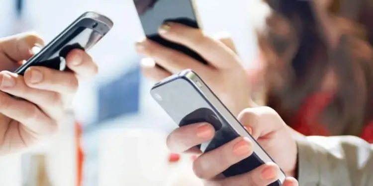 Primer plano de varias personas usando teléfonos inteligentes simultáneamente en un entorno profesional.