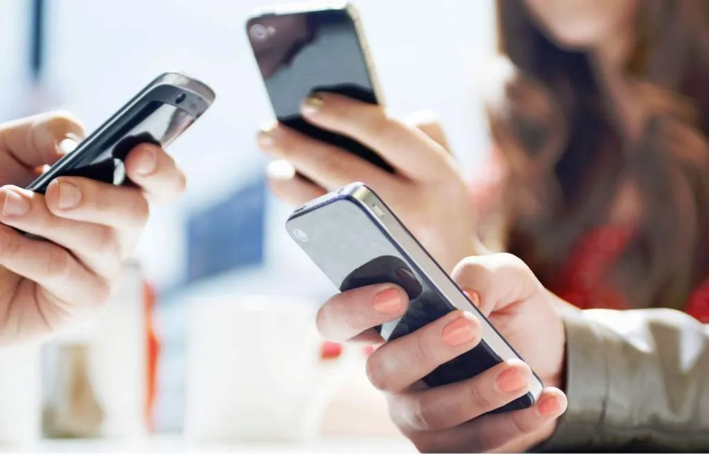 Primer plano de varias personas usando teléfonos inteligentes simultáneamente en un entorno profesional.