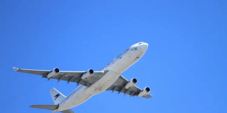 Un gran avión comercial de pasajeros con cuatro motores volando en diagonal contra un cielo azul despejado.