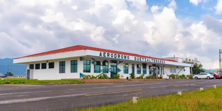 Fachada exterior del edificio del Aeródromo Quetzaltenango bajo un cielo nublado y con una carretera pavimentada al frente.
