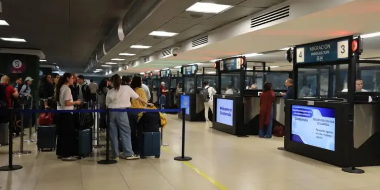 Pasajeros con equipaje esperando en la fila para el control de migración en un aeropuerto.