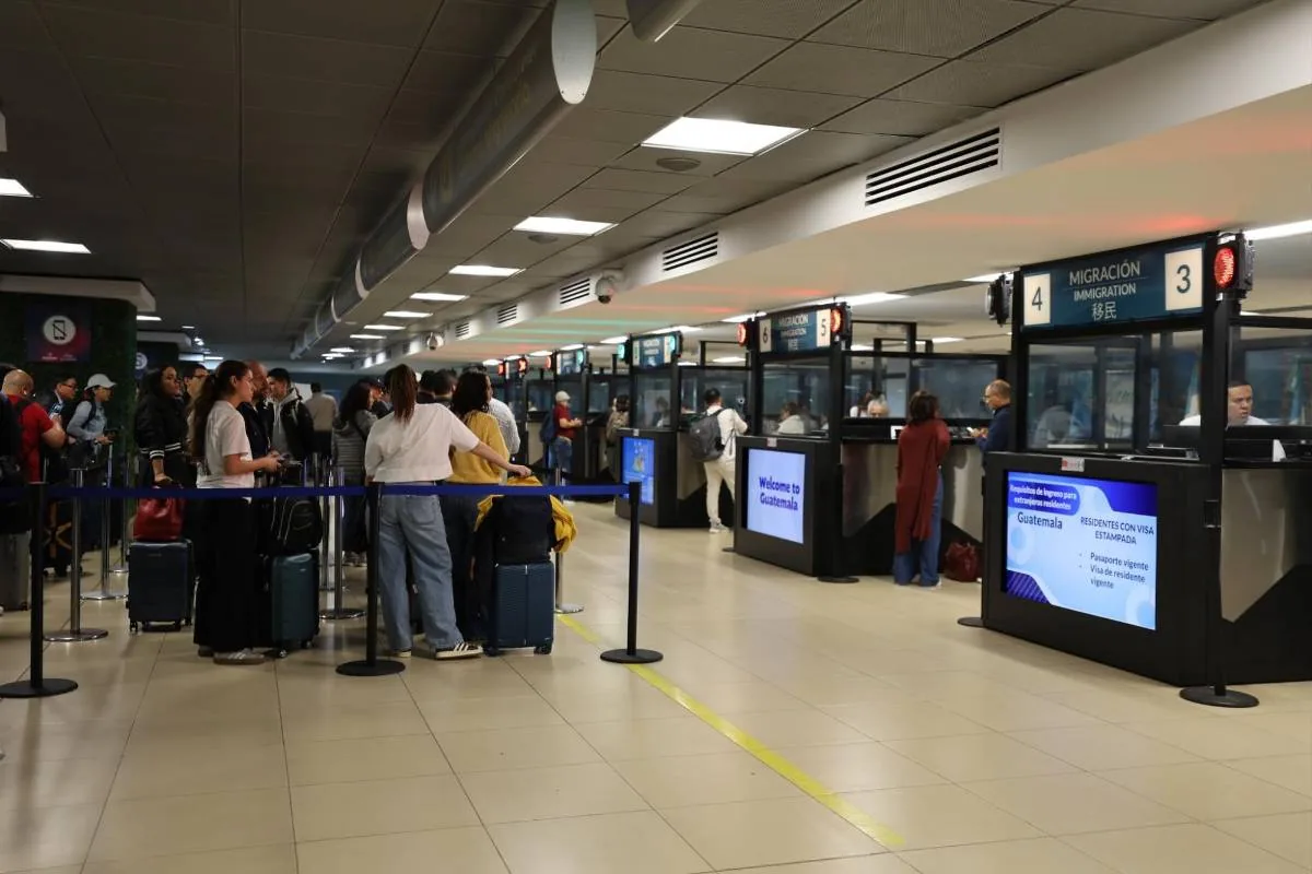 Pasajeros con equipaje esperando en la fila para el control de migración en un aeropuerto.
