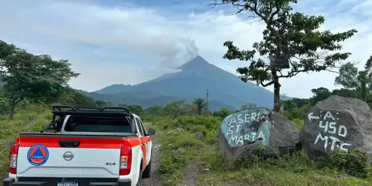 Camioneta Nissan Frontier 4x4 de CONRED Guatemala en camino rural. Volcán humeante al fondo, rocas con 'CASERIO ST MARTA' y 'A: 450 MTS'.