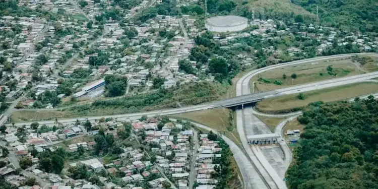 Fotografía aérea que muestra una carretera principal con un peaje, un puente y áreas residenciales densamente pobladas.