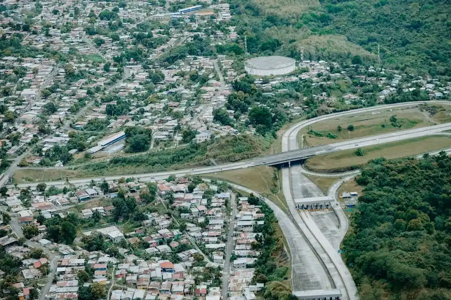 Fotografía aérea que muestra una carretera principal con un peaje, un puente y áreas residenciales densamente pobladas.