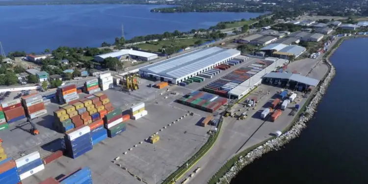 Vista aérea de una terminal portuaria con contenedores de carga apilados junto al mar y bodegas logísticas.
